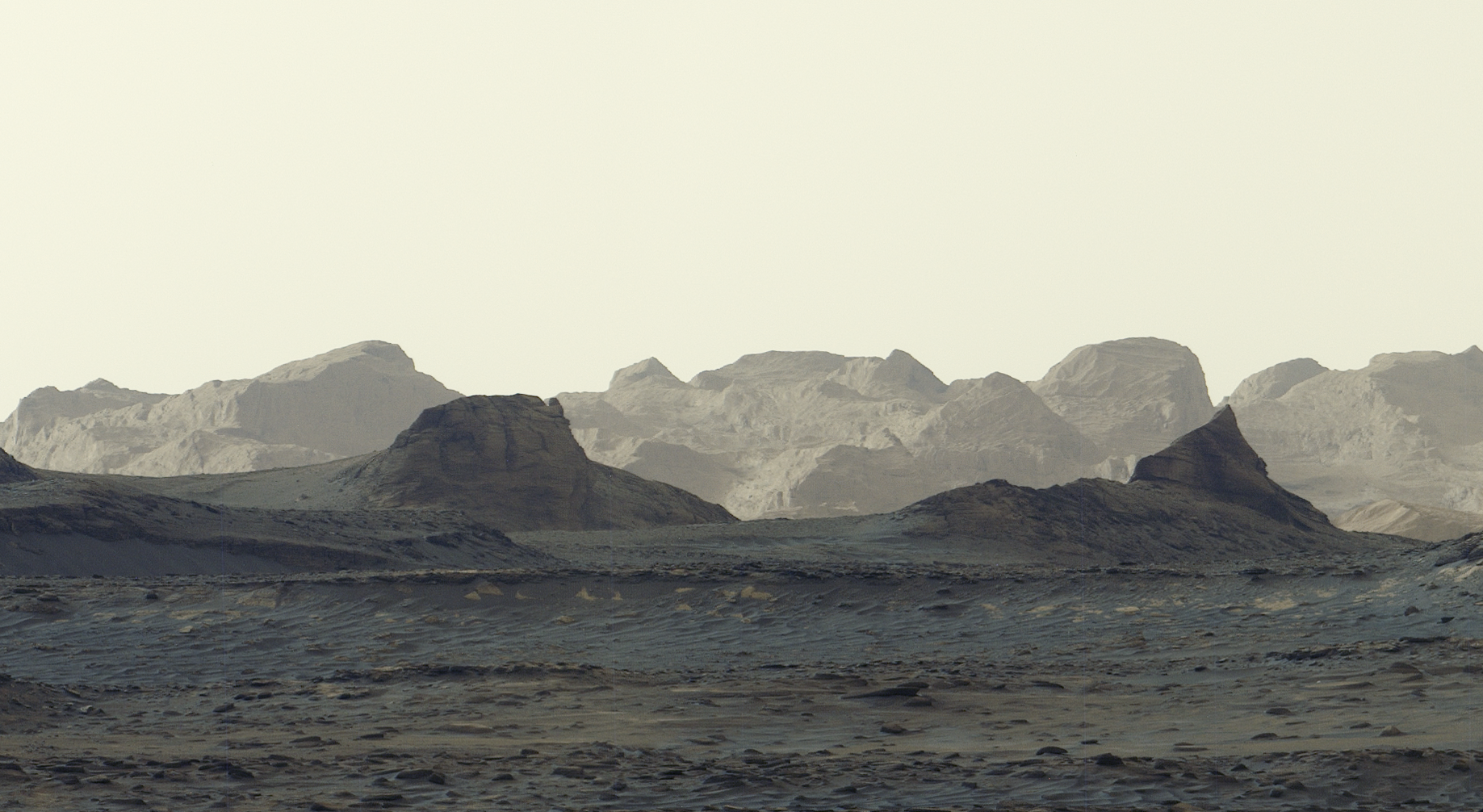 A stark, grayish-tan Martian landscape features jagged rock formations and rolling mountain ridges beneath a pale, hazy sky