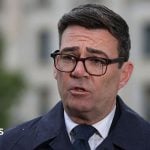 Andy Burnham, wearing a dark suit, recording a media interview in Berlin
