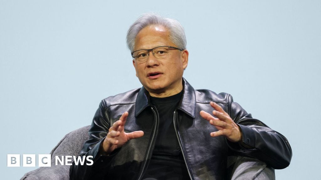 Jensen Huang, the CEO of Nvidia, is seated in a grey armchair against a plain, light-blue background