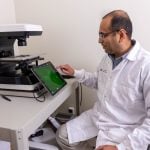 A photo of a researchers in a lab sitting near a machine with a touchscreen monitor