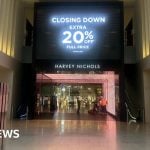 A large black sign is displayed on a digital screen above the entrance to the Harvey Nichols department store at The Mailbox