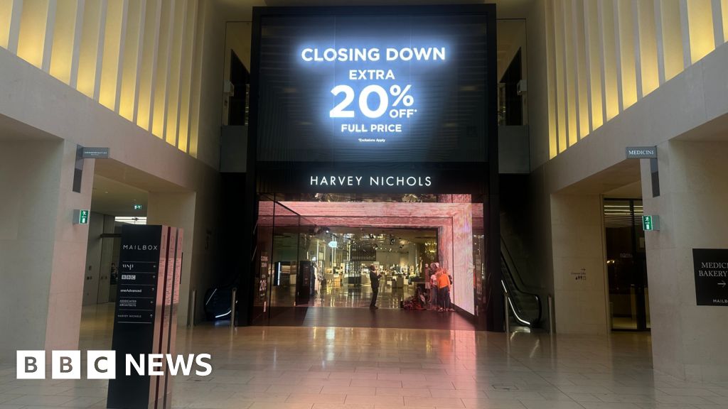 A large black sign is displayed on a digital screen above the entrance to the Harvey Nichols department store at The Mailbox