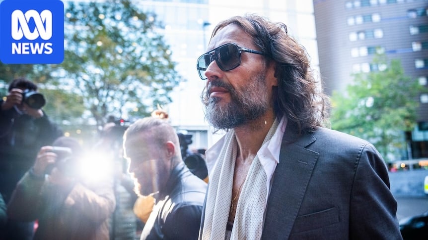 A man in a suit talking and looking on as a camera flashes nearby